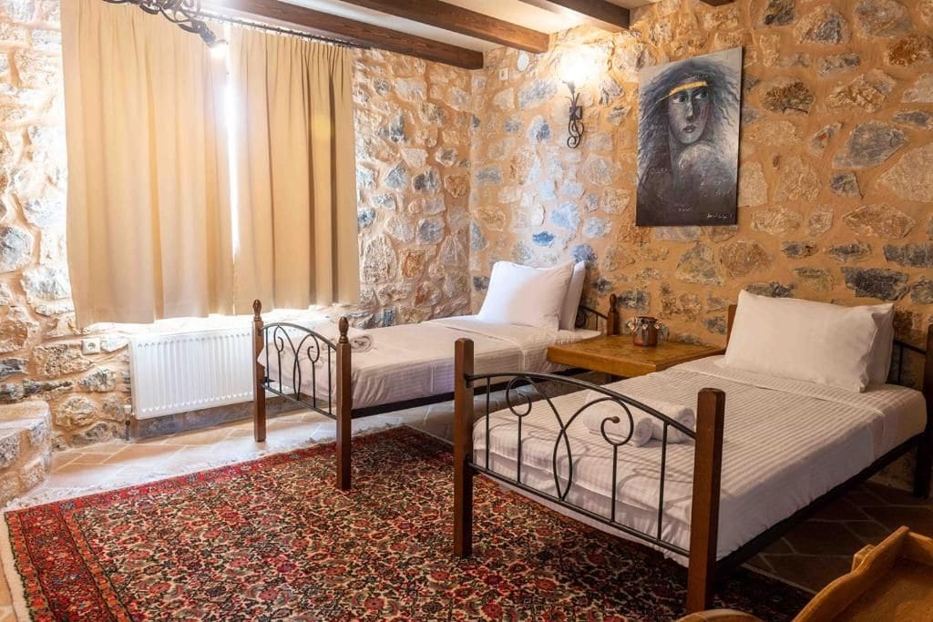 Un dormitorio con dos camas individuales, una pared de piedra, un cuadro y un cabecero de madera.