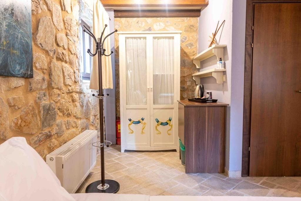 A stone-walled room with a radiator, a coat rack, a white cabinet with colorful handles, and a wooden door.