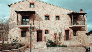 A stone building with a central entrance, two balconies, and a small porch area.