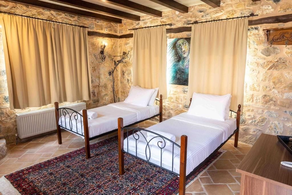 Una habitación con dos camas individuales, una pared de piedra, un radiador y una mesa de madera.