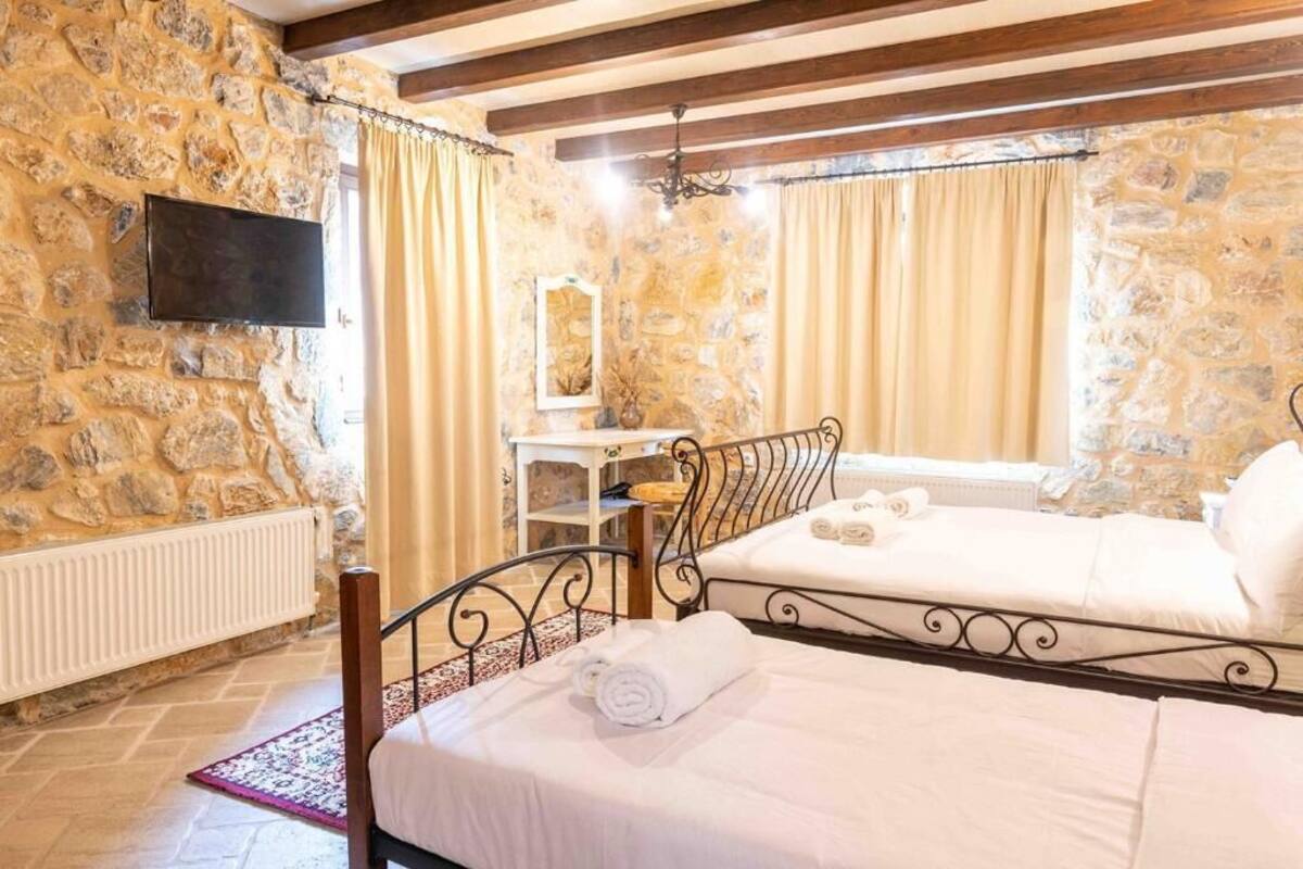 A bedroom with stone walls, a bed with white linens, a bedside table, and a television mounted on the wall.