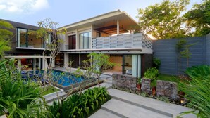 Ein modernes, zweistöckiges Haus mit Pool, Steinmauern und üppiger Bepflanzung.
