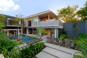 Une maison moderne à deux étages, dotée d’une piscine, de murs en pierre et d’une végétation luxuriante.
