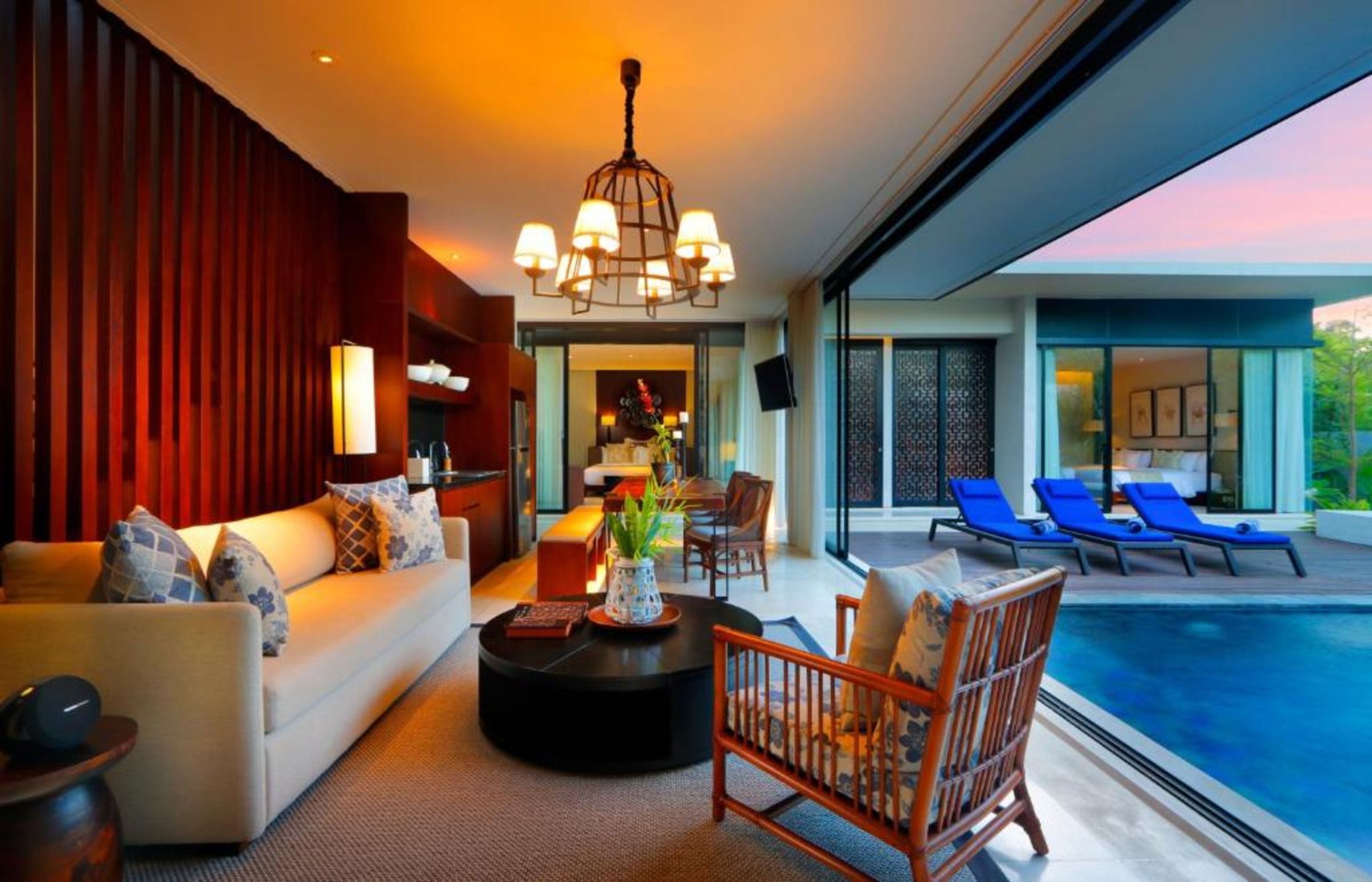 Un salon moderne avec un canapé, une table basse et un espace aménagé près de la piscine, comprenant des chaises longues.