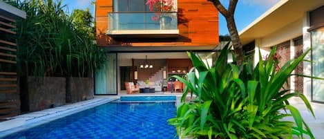 Une maison moderne à deux étages, dotée d’une piscine, d’une façade en bois et d’un balcon agrémenté de fleurs.