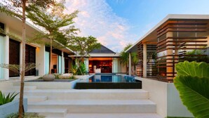 Ein modernes Haus mit Swimmingpool, Treppen, die zum Eingang führen, und ein großer Baum im Vordergrund.