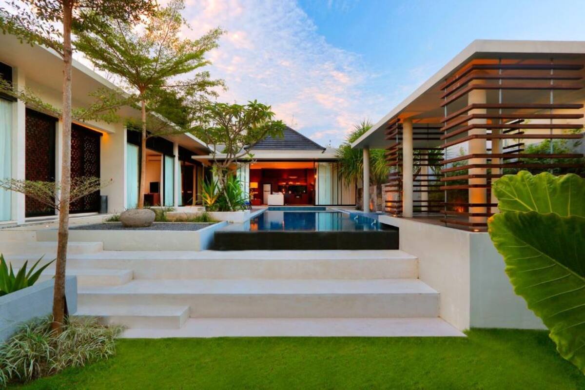 A modern house with a swimming pool, steps leading to the entrance, and a large tree in the foreground.