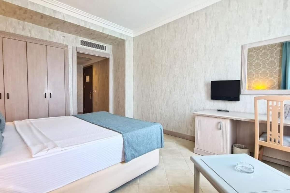 Ein Hotelzimmer mit Bett, Schreibtisch, Stuhl, Fernseher und Kleiderschrank.