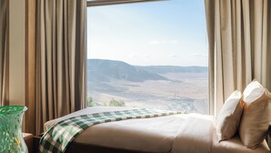 A hotel room with a large window, a bed with a checkered blanket, and a view of a mountainous landscape. - Ngorongoro Lodge Melia Collection (Ngorongoro)