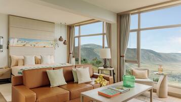 A modern hotel room with a large bed, a sofa, a coffee table, and a view of the mountains.