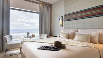 Quarto de hotel com uma cama grande, vista para a cidade, escrivaninha com abajur e uma cadeira.