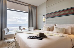 A hotel room with a large bed, a view of the city, a desk with a lamp, and a chair. - Ngorongoro Lodge Melia Collection (Ngorongoro)