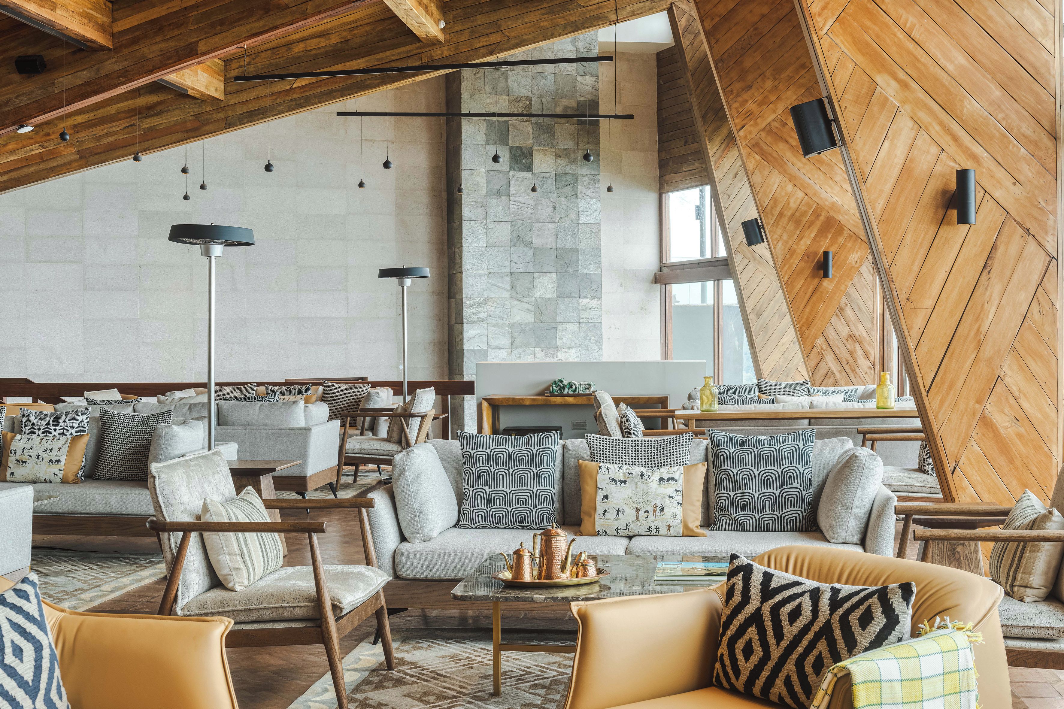 A modern interior with a high ceiling, exposed wooden beams, and a mix of seating arrangements including sofas and chairs.