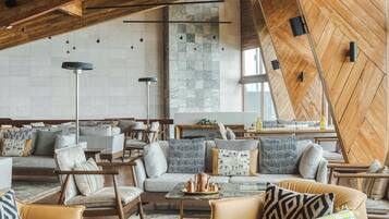A modern interior with a high ceiling, exposed wooden beams, and a mix of seating arrangements including sofas and chairs.