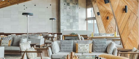 A modern interior with a high ceiling, exposed wooden beams, and a mix of seating arrangements including sofas and chairs.