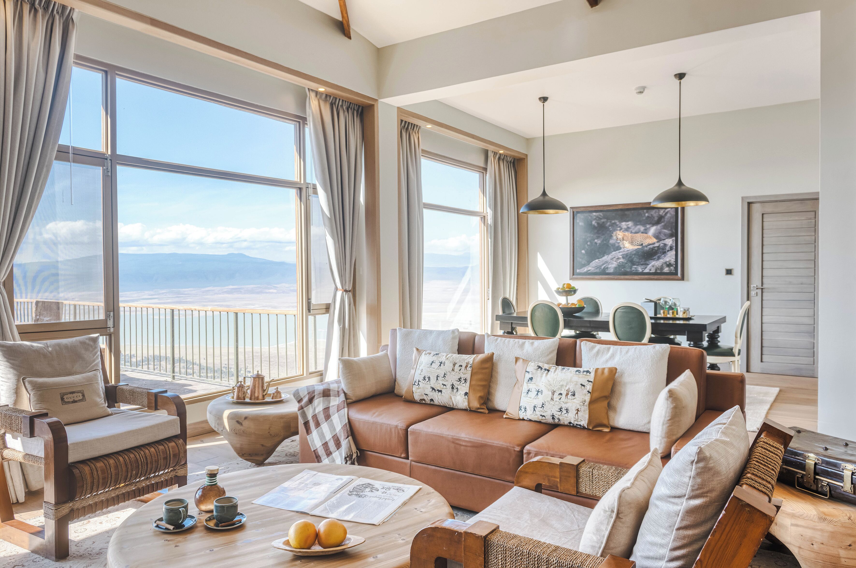 A spacious living room with a large window offering a view of the mountains, a cozy brown leather sofa, and a dining area with a table and chairs.