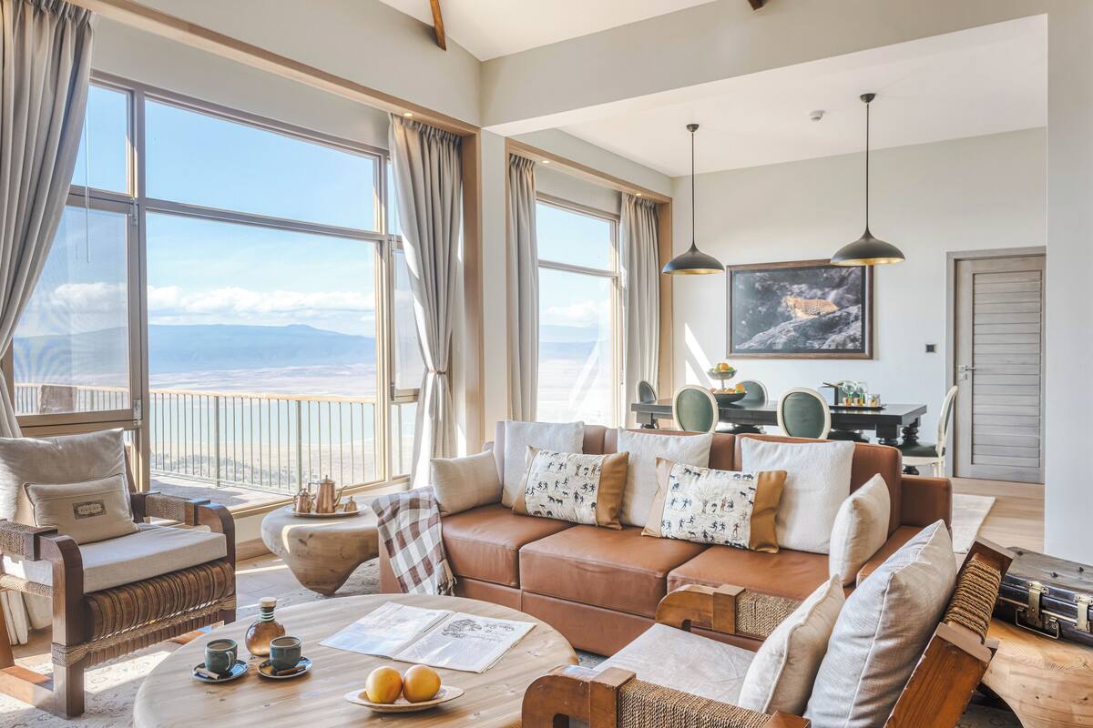 A spacious living room with a large window offering a view of the mountains, a cozy brown leather sofa, and a dining area with a table and chairs.