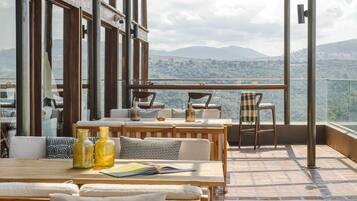 Um terraço com mobiliário de madeira, vista para montanhas e guarda-corpo de vidro.