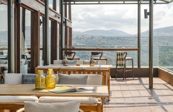 A terrace with wooden furniture, a view of mountains, and a glass railing. - Ngorongoro Lodge Melia Collection (Ngorongoro)