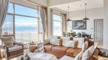 A spacious living room with a large window offering a view of the mountains, a cozy brown leather sofa, and a dining area with a table and chairs.