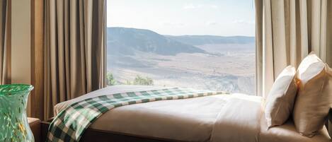 Habitación de hotel con un ventanal grande, una cama con manta a cuadros y vistas a un paisaje montañoso.
