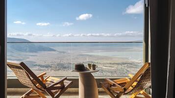 A balcony with two wooden lounge chairs and a small table, overlooking a scenic landscape with mountains and a body of water.