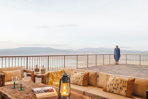 A terrace with a sofa, a wooden table, and a lantern. - Ngorongoro Lodge Melia Collection (Ngorongoro)