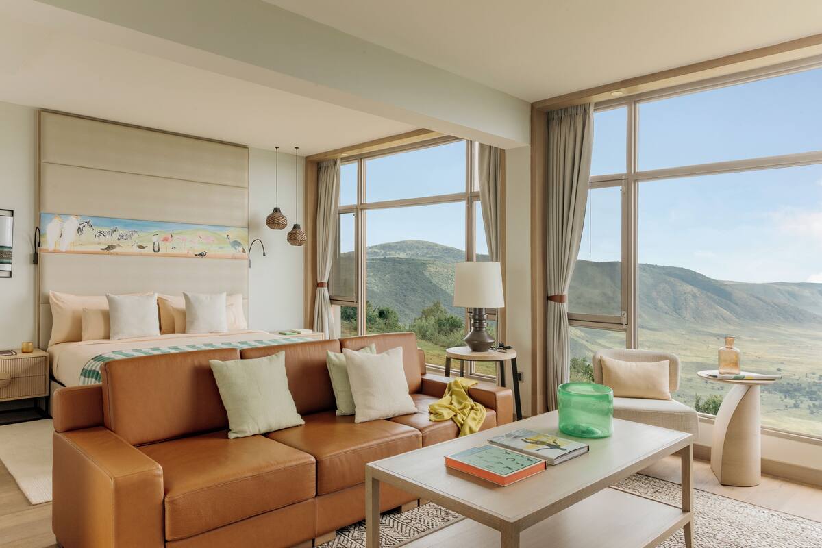 A modern hotel room with a large bed, a sofa, a coffee table, and a view of the mountains.