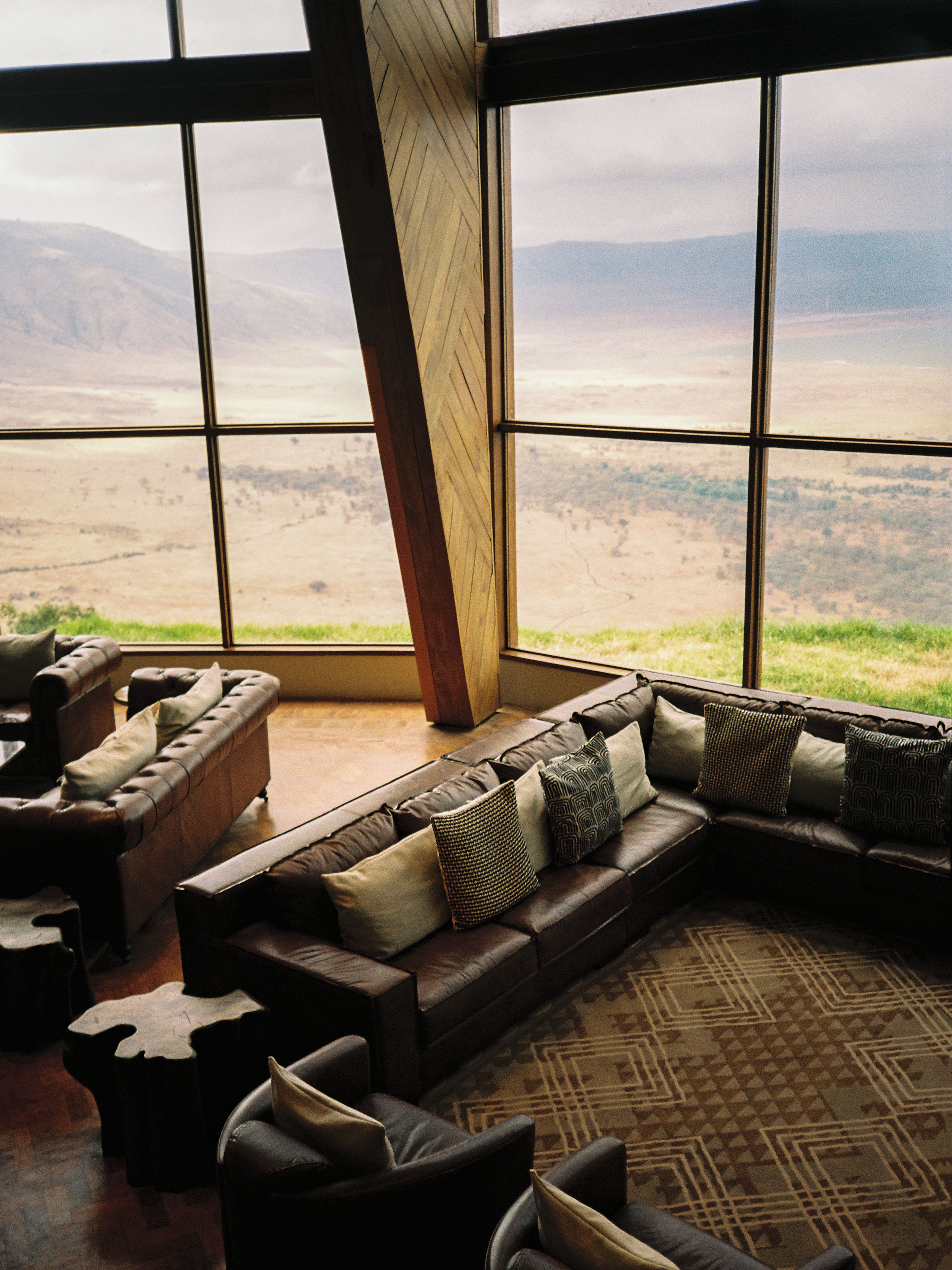 A room with a large window offering a view of a landscape. There is a sectional sofa with multiple cushions.