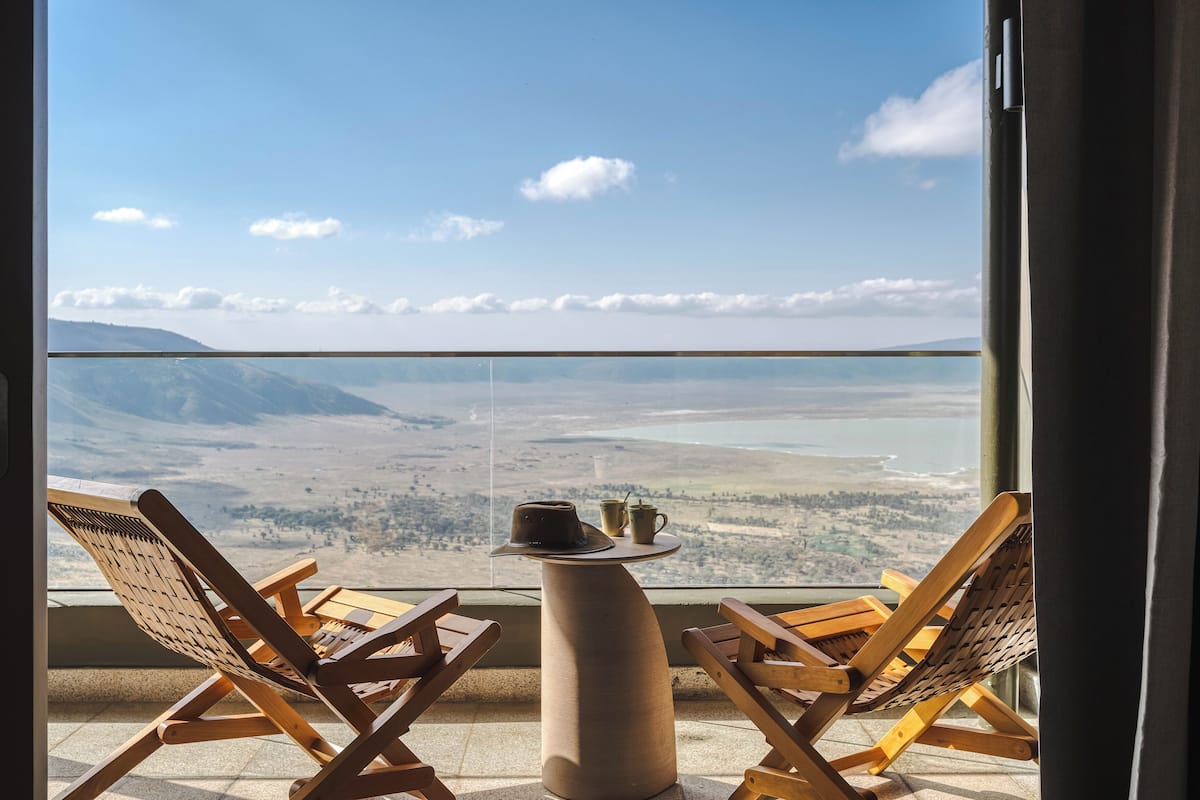 A balcony with two wooden lounge chairs and a small table, overlooking a scenic landscape with mountains and a body of water.