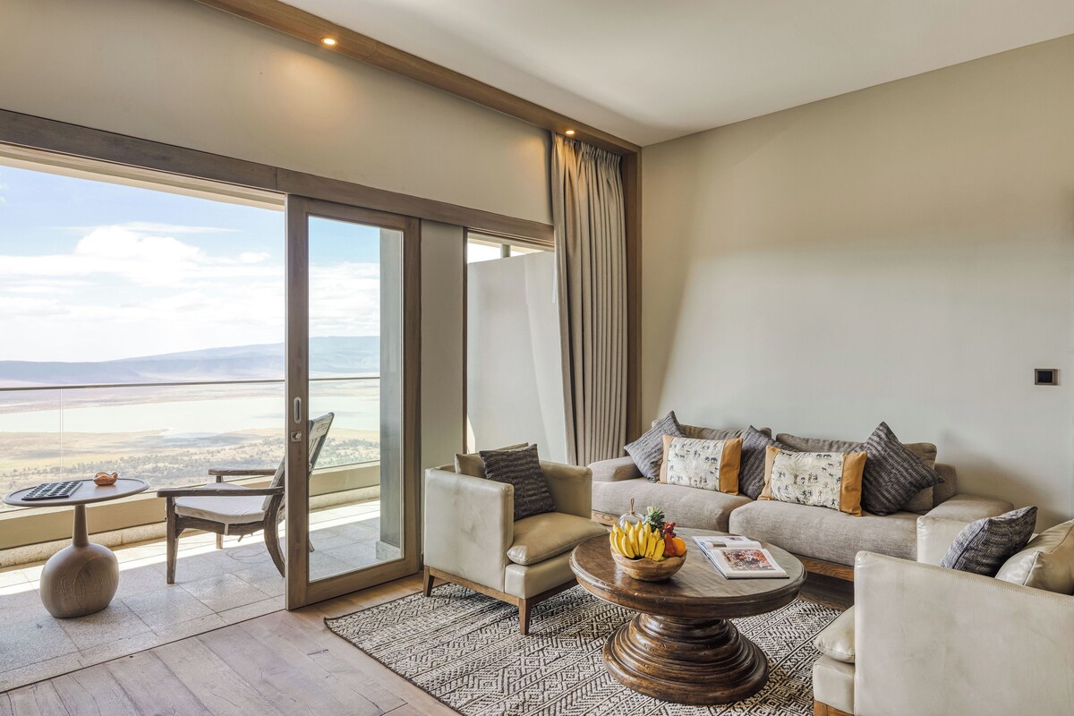 A spacious living room with a sofa, armchairs, a coffee table, and a view of the landscape through large windows.