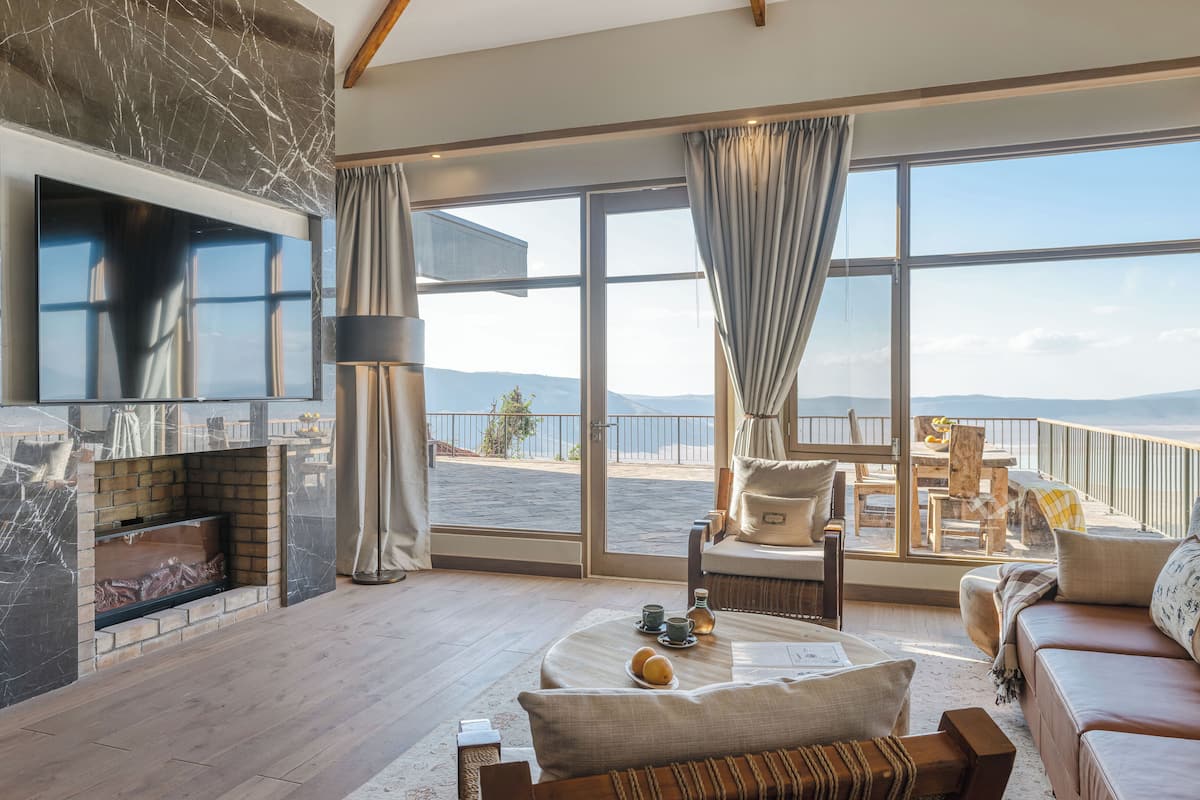 A spacious living room with a large TV, a fireplace, and a balcony with a view of the sea.