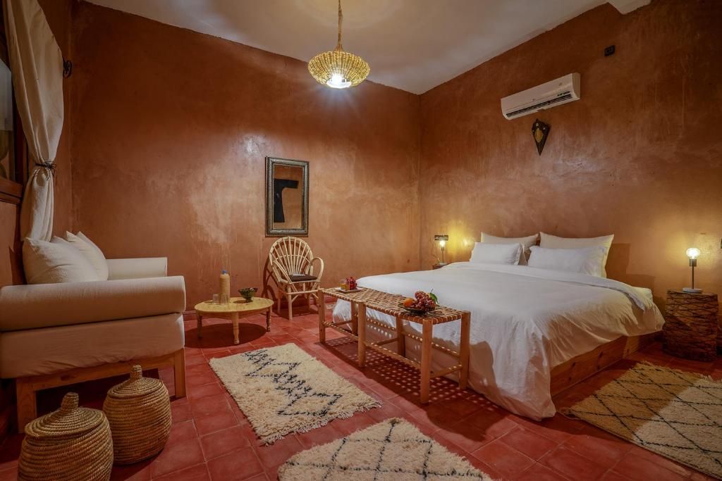 Un dormitorio con cama, una silla, una mesita y una lámpara colgante.