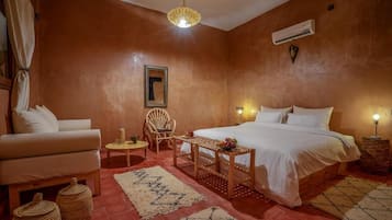 Un dormitorio con cama, una silla, una mesita y una lámpara colgante.