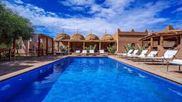 Una piscina con sillas de descanso y un pabellón con techos abovedados.