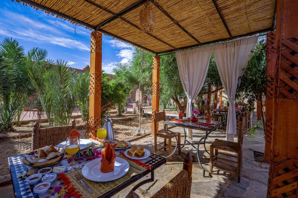 Un espacio de comedor al aire libre con mesas, sillas y una sección cubierta con techo de paja.