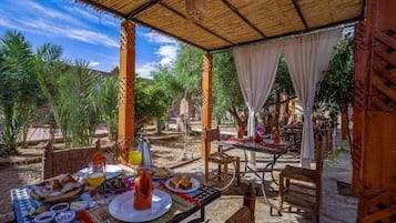 Un espacio de comedor al aire libre con mesas, sillas y una sección cubierta con techo de paja.
