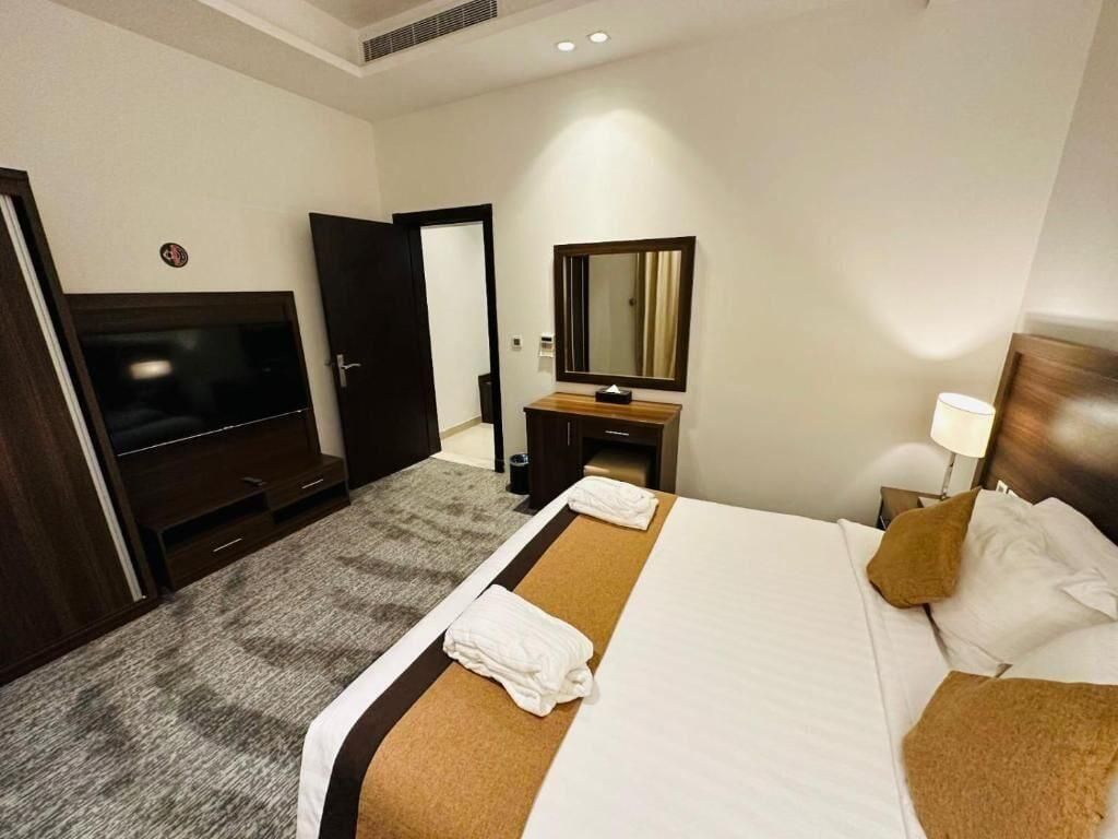 A hotel room with a bed, a TV, a mirror, a desk, and a lamp.