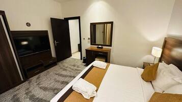A hotel room with a bed, a TV, a mirror, a desk, and a lamp.