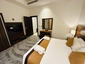 A hotel room with a bed, a TV, a mirror, a desk, and a lamp. - Seiba Hotel (Riyadh)