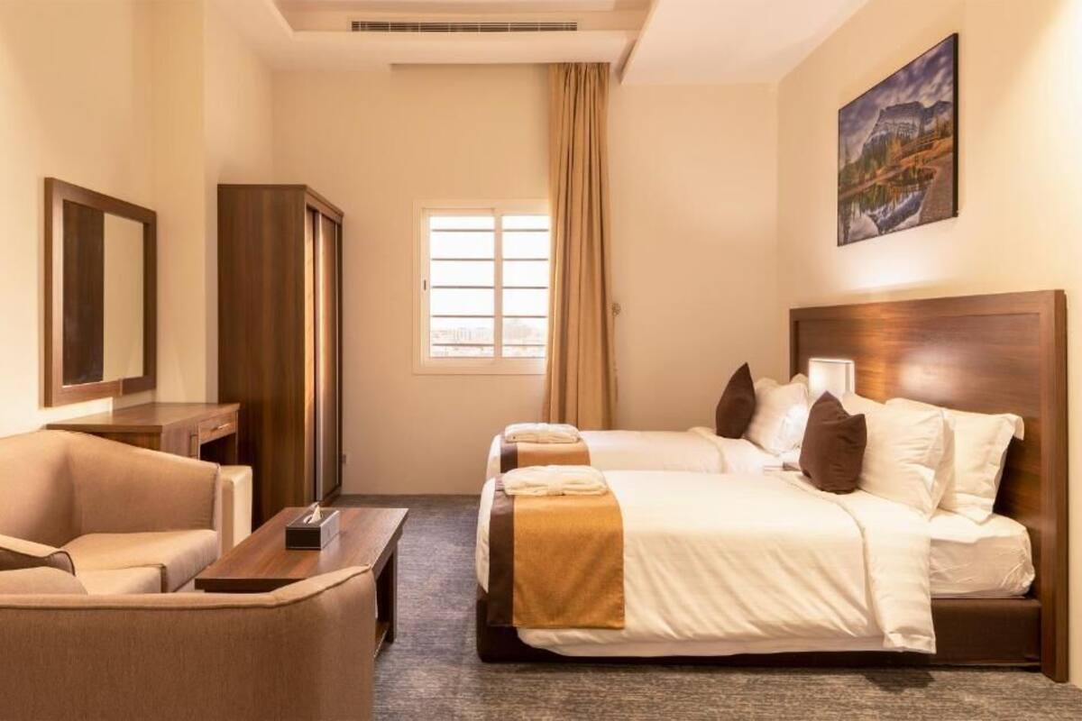 Habitación de hotel con dos camas, un sofá, un escritorio y un ventanal grande.