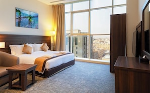 A hotel room with a large bed, a sofa, a TV, and a city view through the window. - Seiba Hotel (Riyadh)
