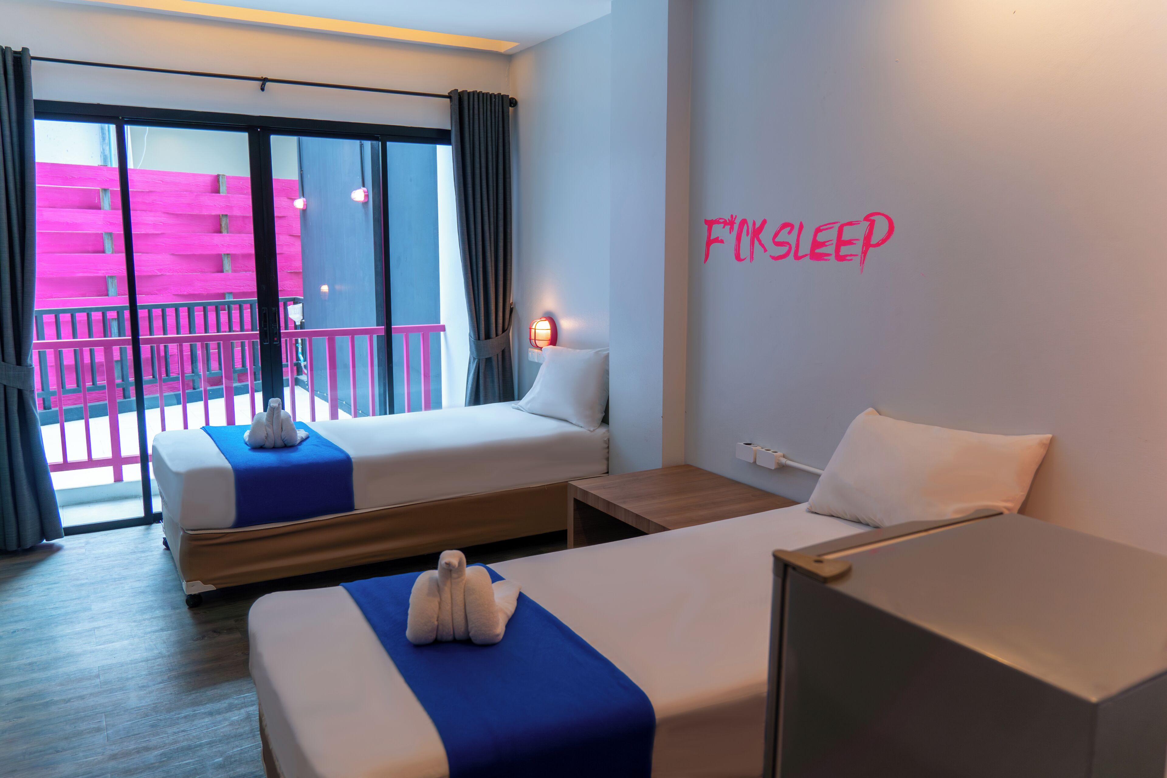 Habitación de hotel con dos camas, un balcón y un letrero de neón en la pared.