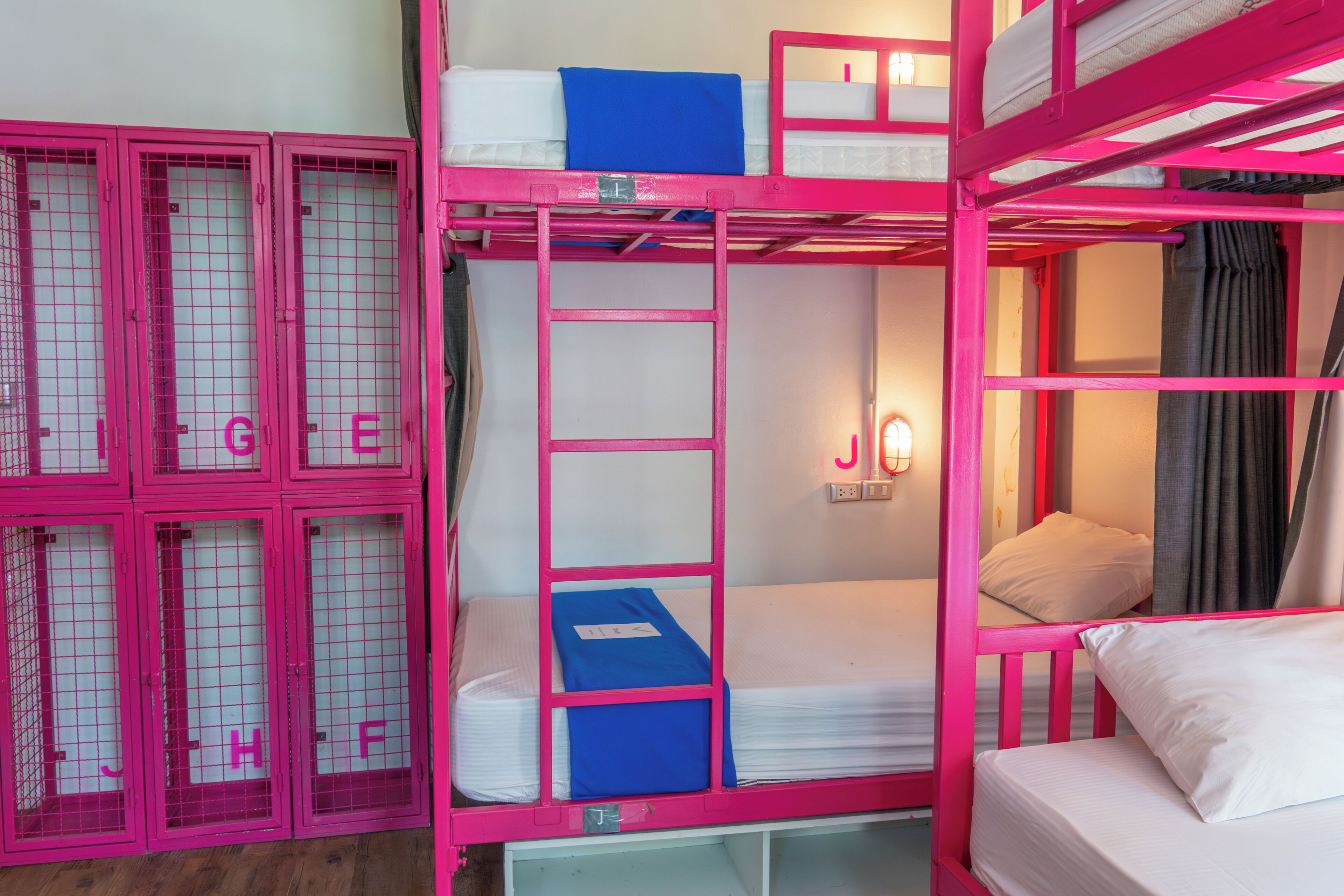 Habitación con literas de barandillas metálicas rosas, colchón blanco y almohada azul.