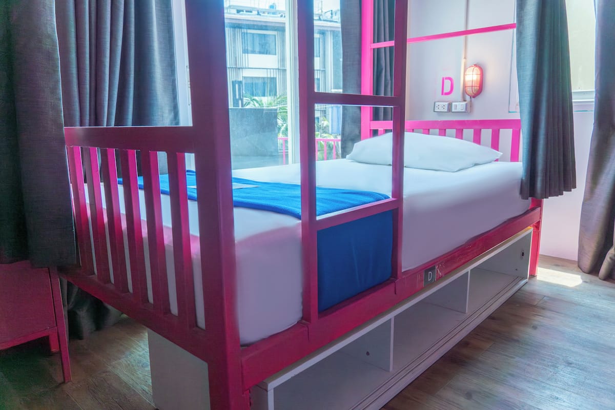 Una cama litera con estructura rosa, colchón blanco y manta azul.