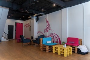 Une pièce avec un plancher en bois, un rideau rouge, des chaises bleues et rouges, une table jaune et un mur orné d’une fresque rouge.