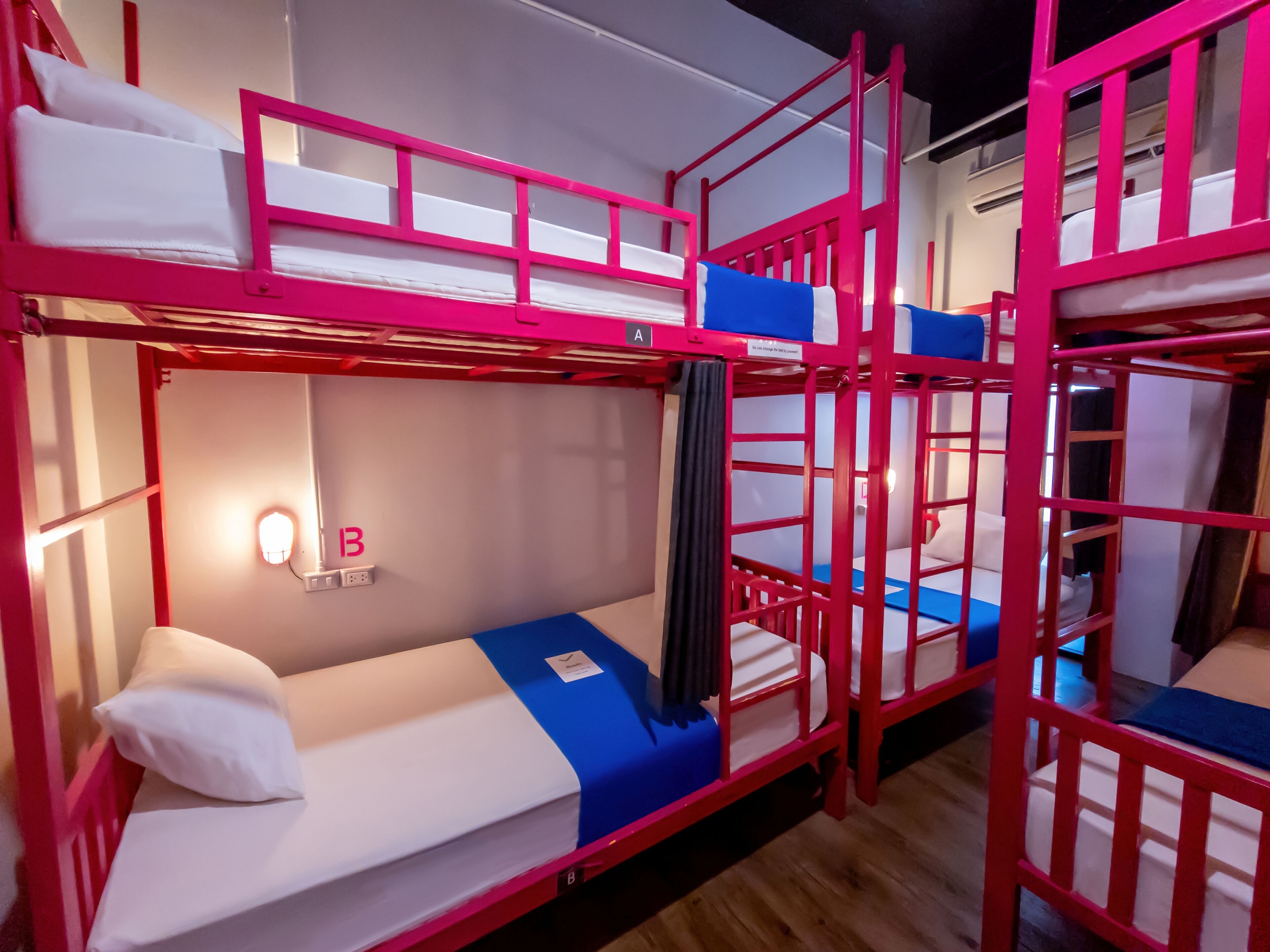 Habitación con literas, una lámpara, un enchufe en la pared y una etiqueta en el colchón.