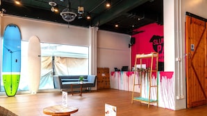 A room with a large window, a surfboard, a sofa, a small table, and a wooden door.