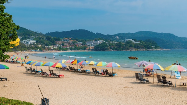 A beach with rows of sun loungers and umbrellas, a clear view of the ocean, and a hilly landscape in the background.