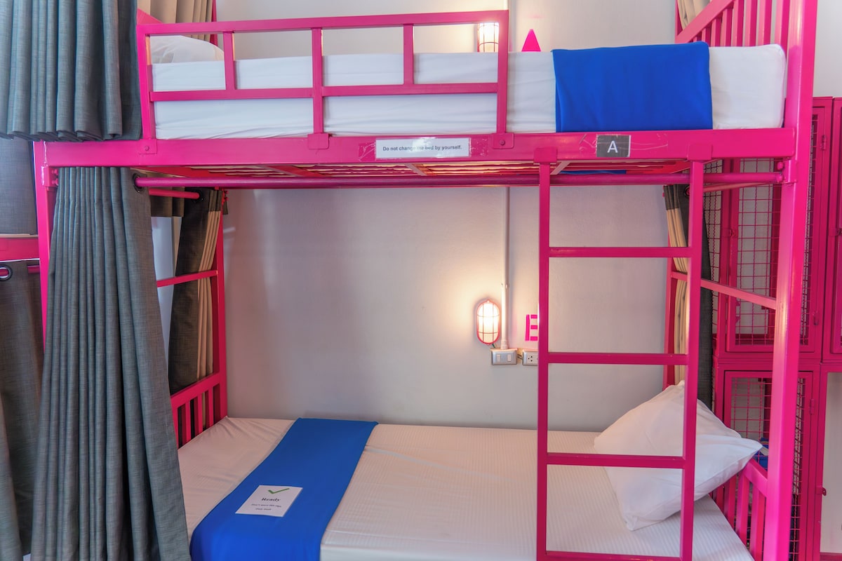 A bunk bed with a sign on the top bunk, a wall-mounted light, and a curtain.